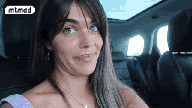 a woman is sitting in a car with a mtmad logo in the background
