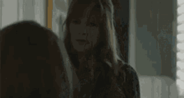 a woman is looking at herself in the mirror in a dark room .
