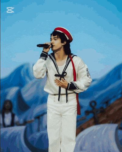 a man in a sailor 's uniform sings into a microphone