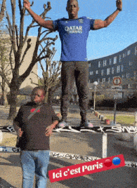 a man wearing a blue qatar airways shirt stands on a fence