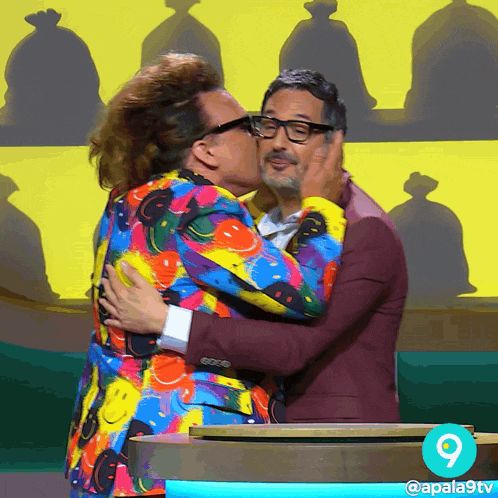 a man in a colorful suit is kissing another man in a purple suit