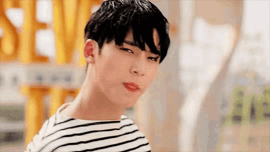 a young man wearing a striped shirt is making a funny face and looking at the camera .