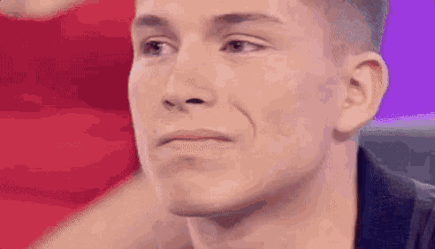 a close up of a man 's face with a purple background and a red shirt in the background .