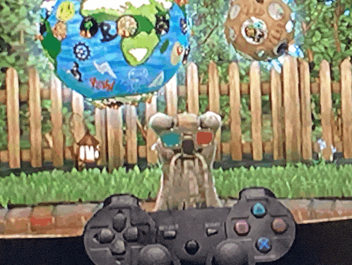 a video game controller is sitting in front of a fence and a balloon that says yow on it