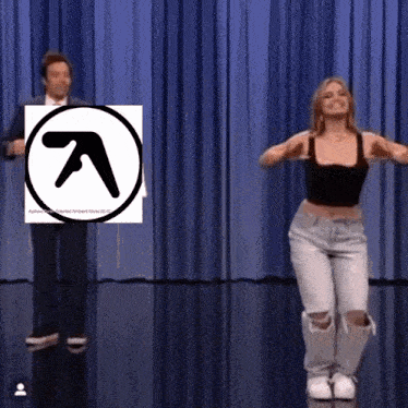 a man and a woman are dancing in front of a blue curtain with an a logo in the background