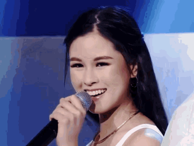 a woman is singing into a microphone with a smile on her face
