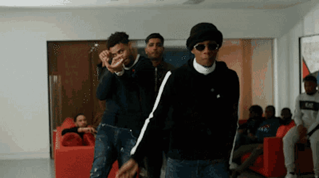 a group of men are standing in a living room with a red couch in the background