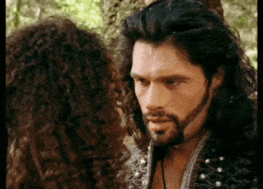 a man with long hair and a beard is standing next to a woman with curly hair .