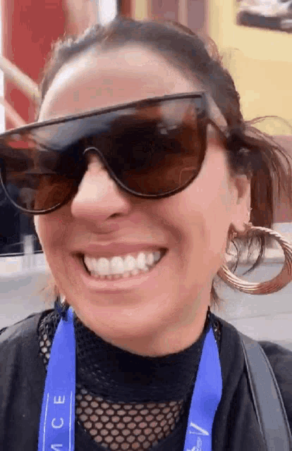 a woman wearing sunglasses and hoop earrings smiles