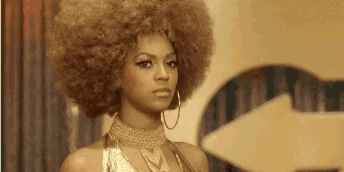 a woman with a large afro is wearing a gold dress and hoop earrings .