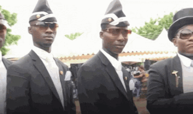 a group of men in black suits and hats are standing in a line .