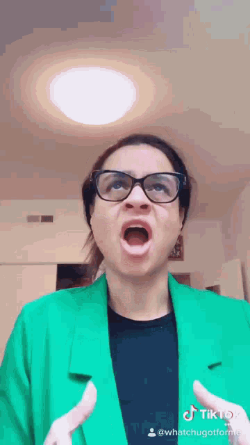 a woman wearing glasses and a green jacket is making a funny face on a tiktok video