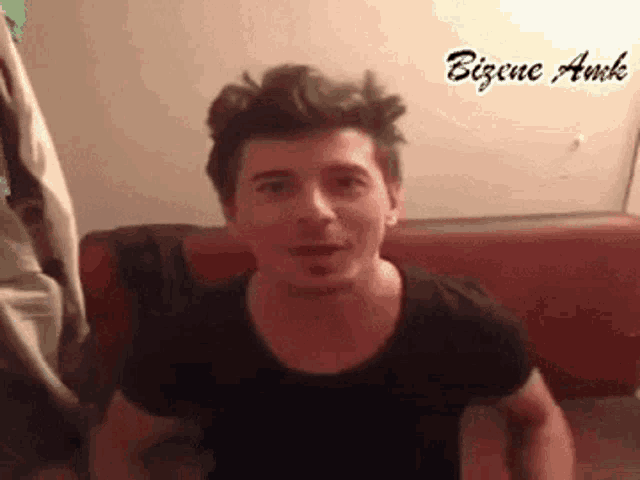 a man in a black shirt is sitting on a red couch and making a face