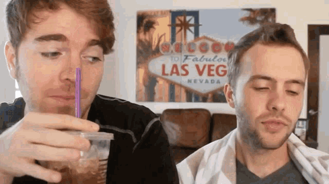 two men drinking from plastic cups in front of a sign that says las veg nevada