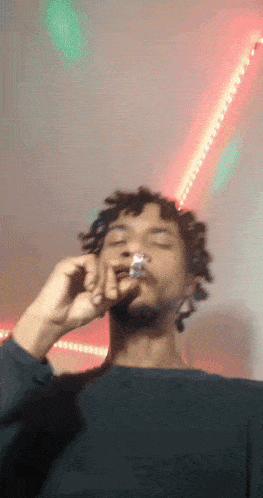a man with dreadlocks is smoking a cigarette in front of a pink and green background