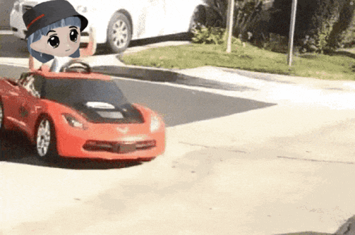 a little girl is driving a red toy car on the street