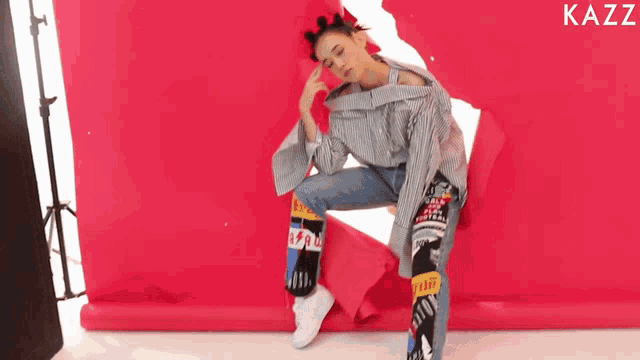 a woman sitting in front of a red background with kazz written on the bottom
