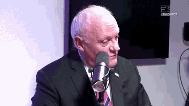 a man in a suit and tie is talking into a microphone with a screen behind him that says fire on es