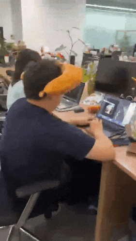 a man wearing a banana hat sits at a desk with a laptop