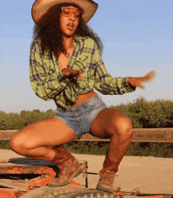 a woman wearing a cowboy hat and shorts squatting on a tire
