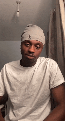 a man wearing a white t-shirt and a grey beanie with the letter a on it