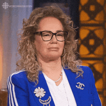 a woman with curly hair wearing glasses and a blue jacket with a chanel brooch