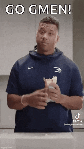 a man in a blue shirt is holding a sandwich in his hands and making a funny face .