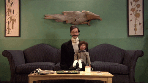 a man in a tuxedo is sitting on a couch with a puppet