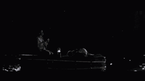 a man sits on a dock with a lantern in the dark