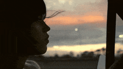 a woman is looking out a window at sunset