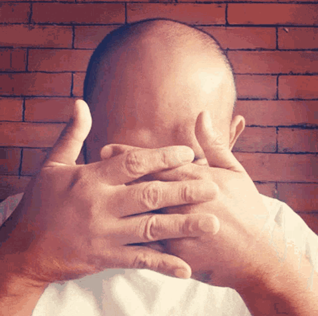a bald man is covering his face with his hands
