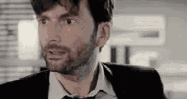 a man with a beard is wearing a suit and tie and making a surprised face .