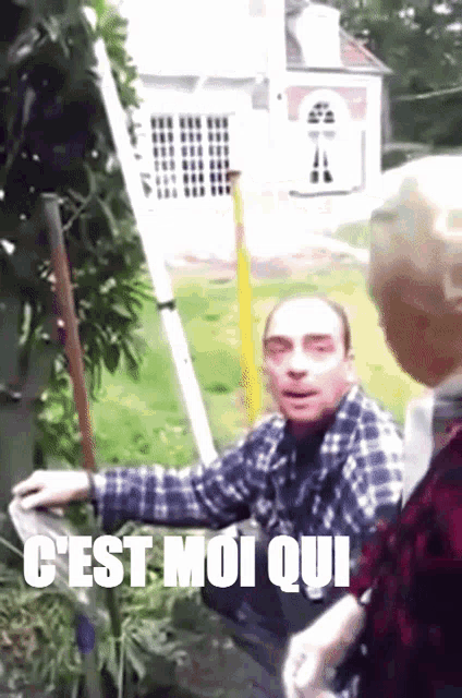 a man in a plaid shirt is standing in front of a sign that says " c'est moi qui " on it