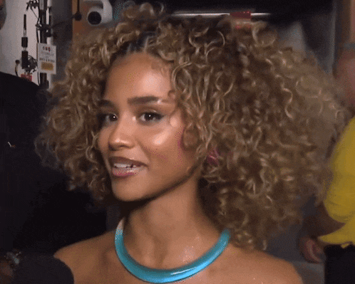 a woman with curly hair is wearing a blue necklace and smiling