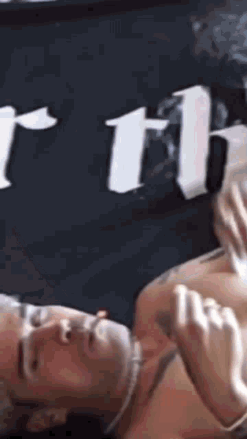 a shirtless man is laying on a bed in front of a sign that says ' rth ' on it .
