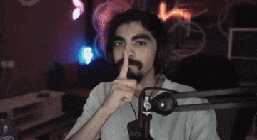a man with a beard is sitting in front of a microphone and making a shhh gesture