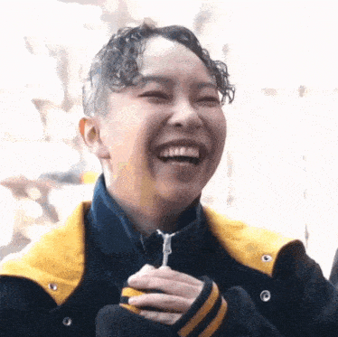 a woman in a yellow and black jacket is laughing while holding a lollipop in her hand .