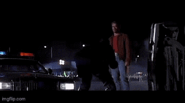 a man in a red shirt is walking down a street at night .
