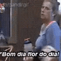 a woman in a blue shirt is standing in front of a mirror holding a water bottle and says bom dia flor do dia .