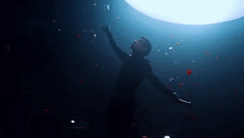 a man is standing in the dark with his arms outstretched in front of a large light