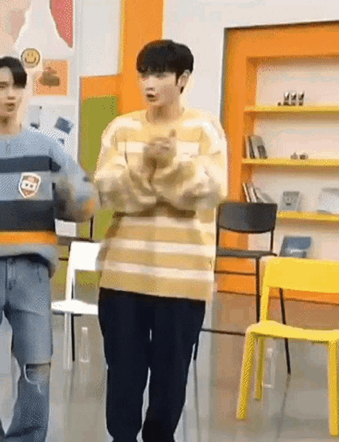 a man in a yellow and black striped sweater is standing in a room with chairs .