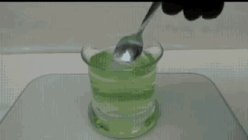 a person is stirring a green liquid with a spoon