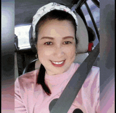 a woman wearing a pink shirt and a headband smiles while sitting in a car