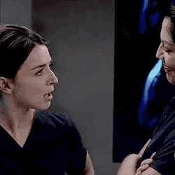 two women in scrubs are talking to each other in a dark room .
