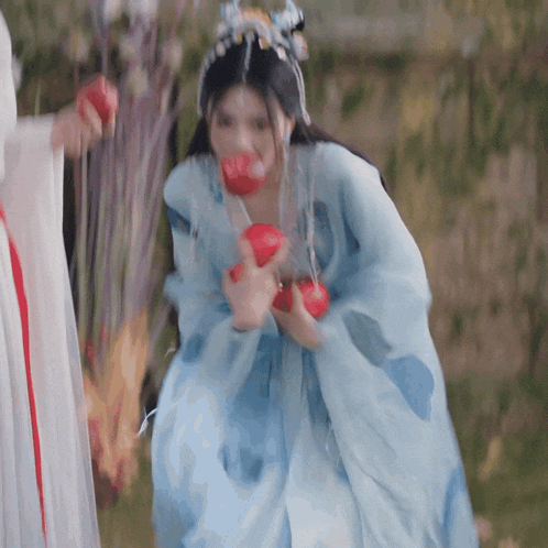 a woman in a blue dress is holding red apples
