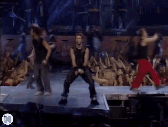 a group of people are dancing on a stage with the letter n on the bottom right