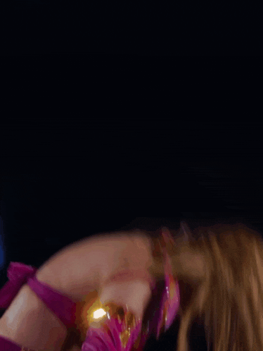 a woman in a pink top is singing into a microphone with her hair blowing in the wind