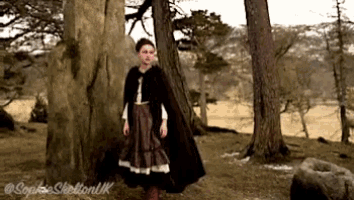 a woman in a cape is standing in the woods and the photo was taken by sophie sheldon uk