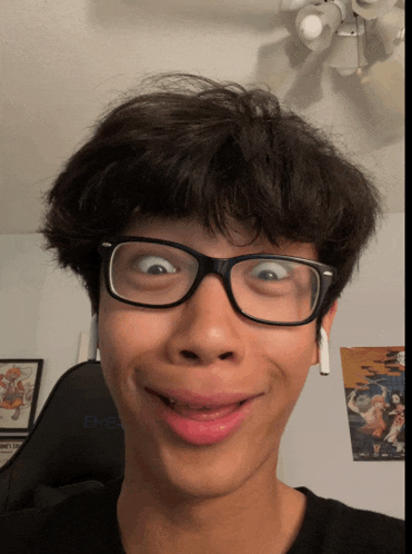 a young man wearing glasses makes a funny face in front of a black emblem chair