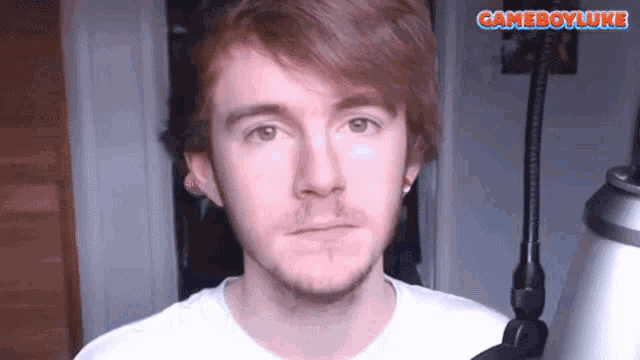 a man in a white shirt stands in front of a microphone with the words gameboyluke above him